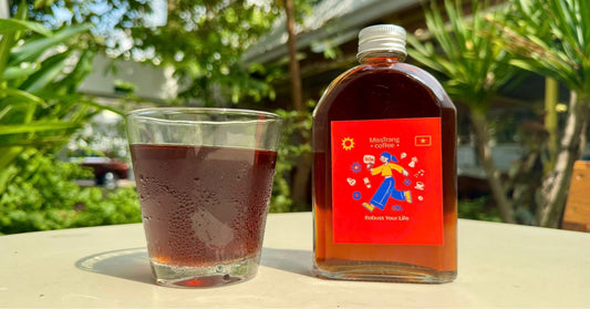 Glass and bottle of cold brew coffee outdoors on a table with lush green background