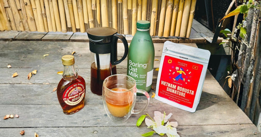 Vietnamese robusta coffee beans, oat milk, maple syrup, and coffee jug on rustic table