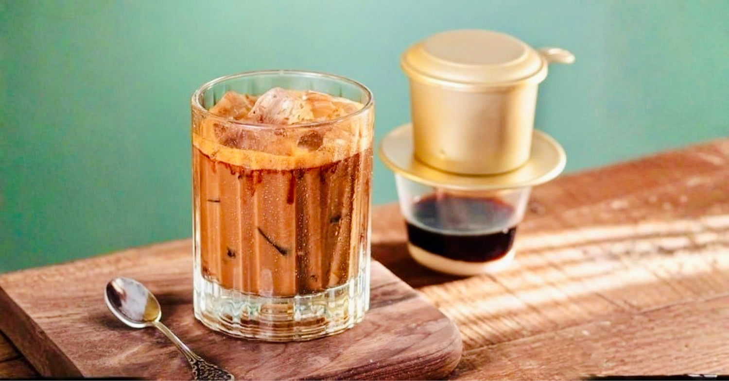 Vietnamese iced coffee with condensed milk in a glass, traditional phin filter beside on wooden table