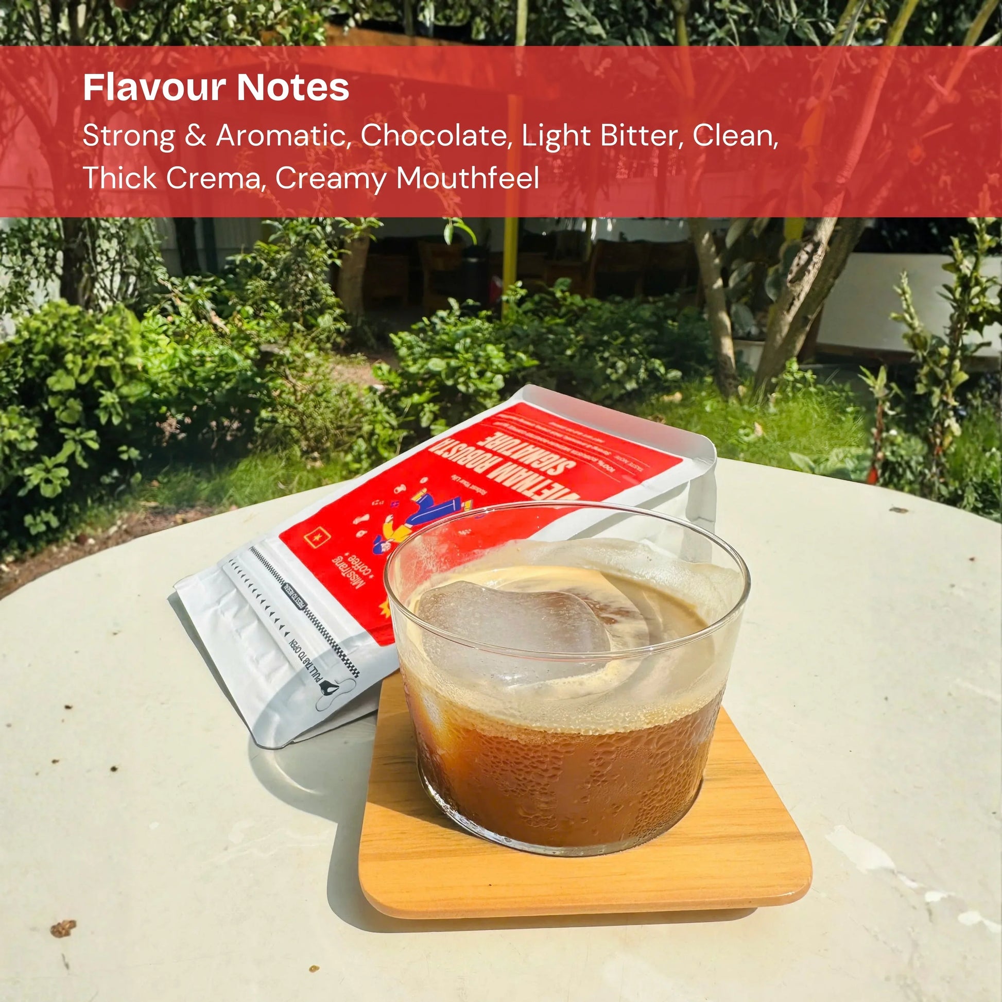Iced coffee with thick crema in a clear glass on a wooden coaster, coffee bag in background, outdoor garden setting