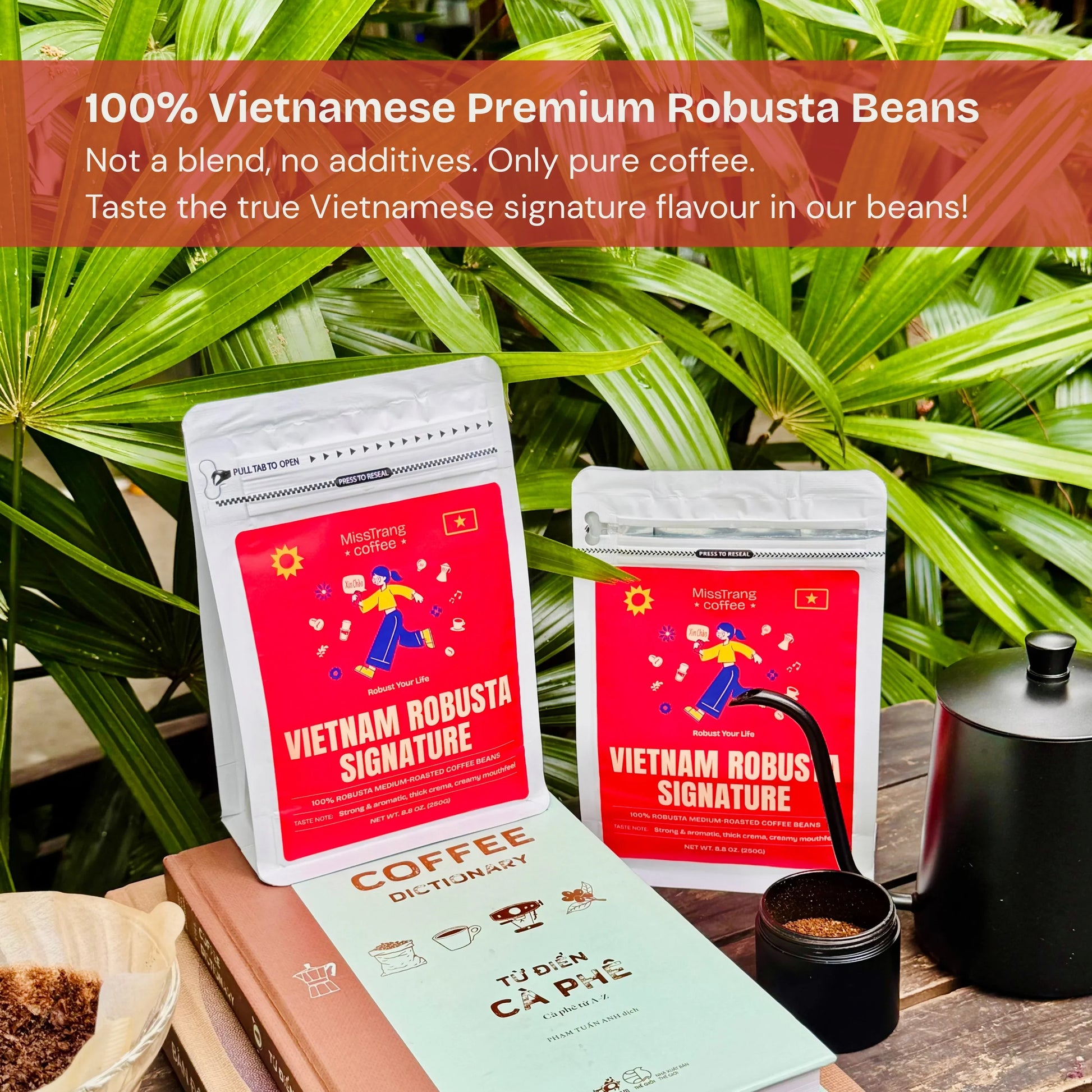 Vietnamese robusta coffee bean bags on table with coffee grinder, coffee dictionary, and lush green leaves