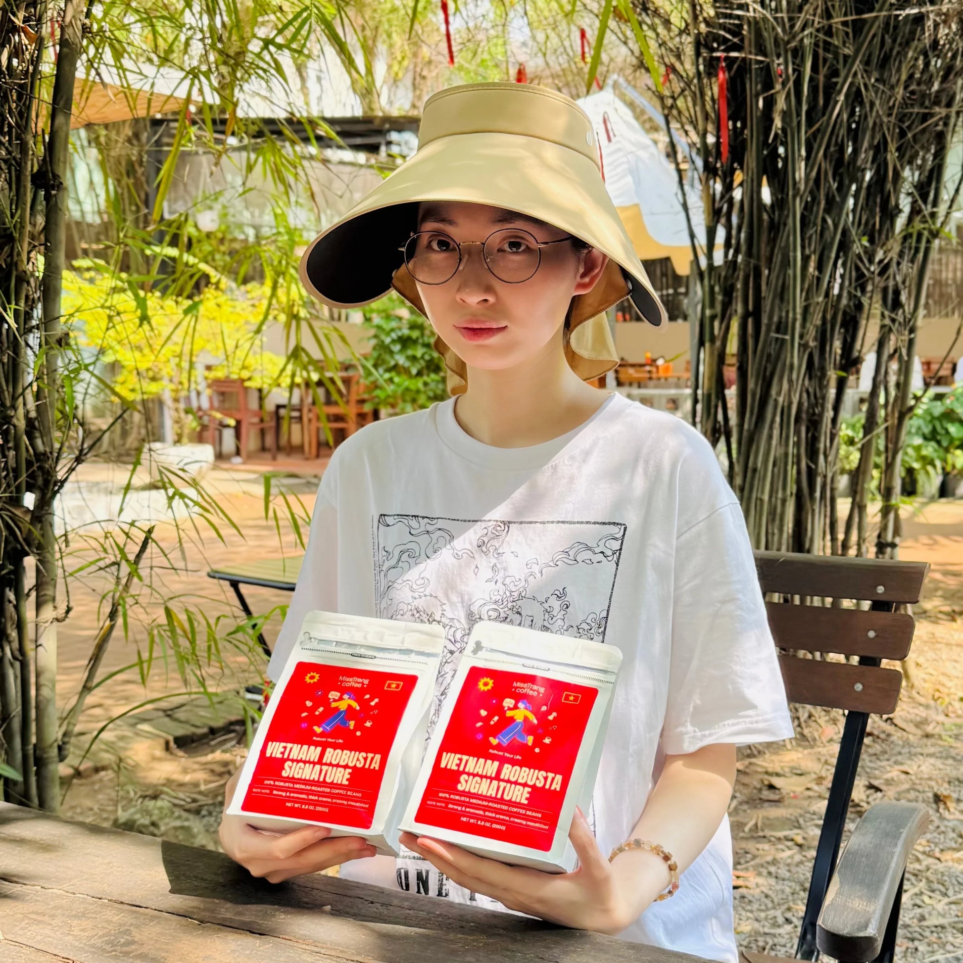 Woman outdoors holding Vietnam Robusta Signature coffee bags at garden café table