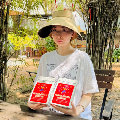 Woman outdoors holding Vietnam Robusta Signature coffee bags at garden café table